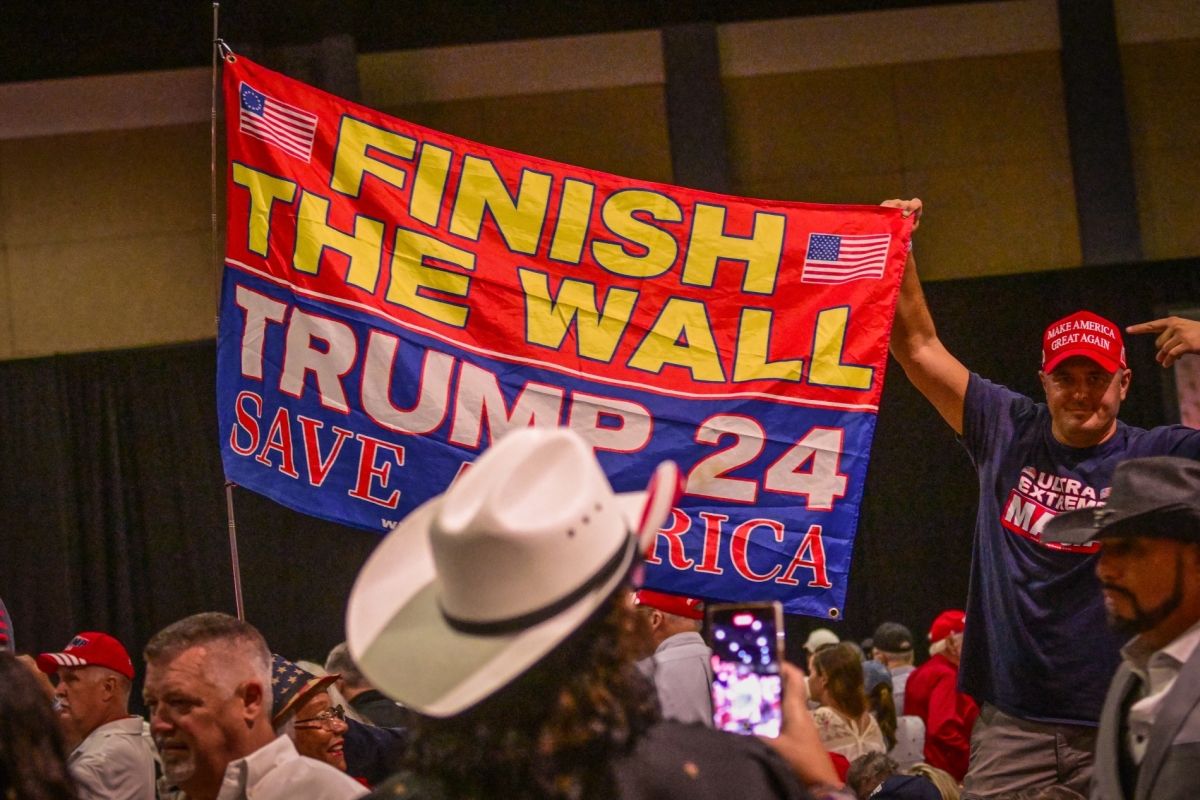 Supporters of Donald Trump hold a sign about the border wall with Mexico before Trump speaks at a campaign rally in Florida on 11 October 2023. Trump has now allocated $46bn to build it.