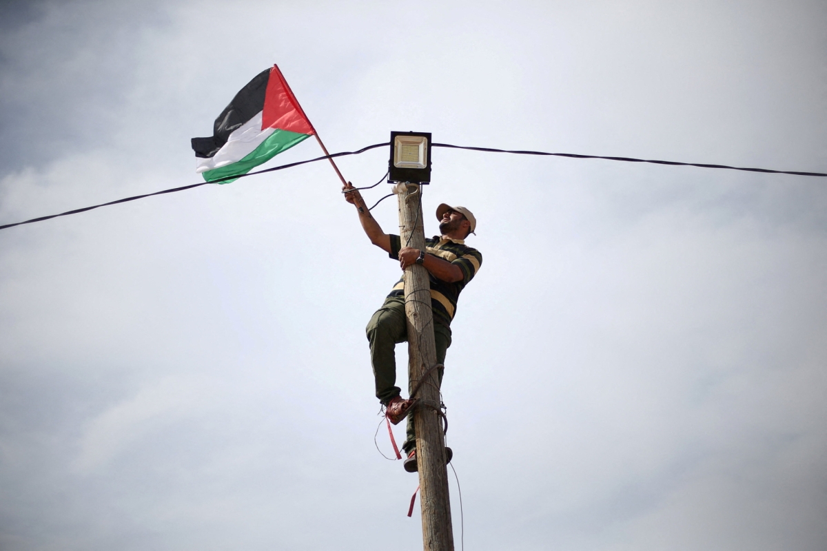 A man hangs a Palestinian flag at an electric pole near the border with Israel, in the southern Gaza Strip, before the recent war that has knocked out most of the territory's infrastructure.