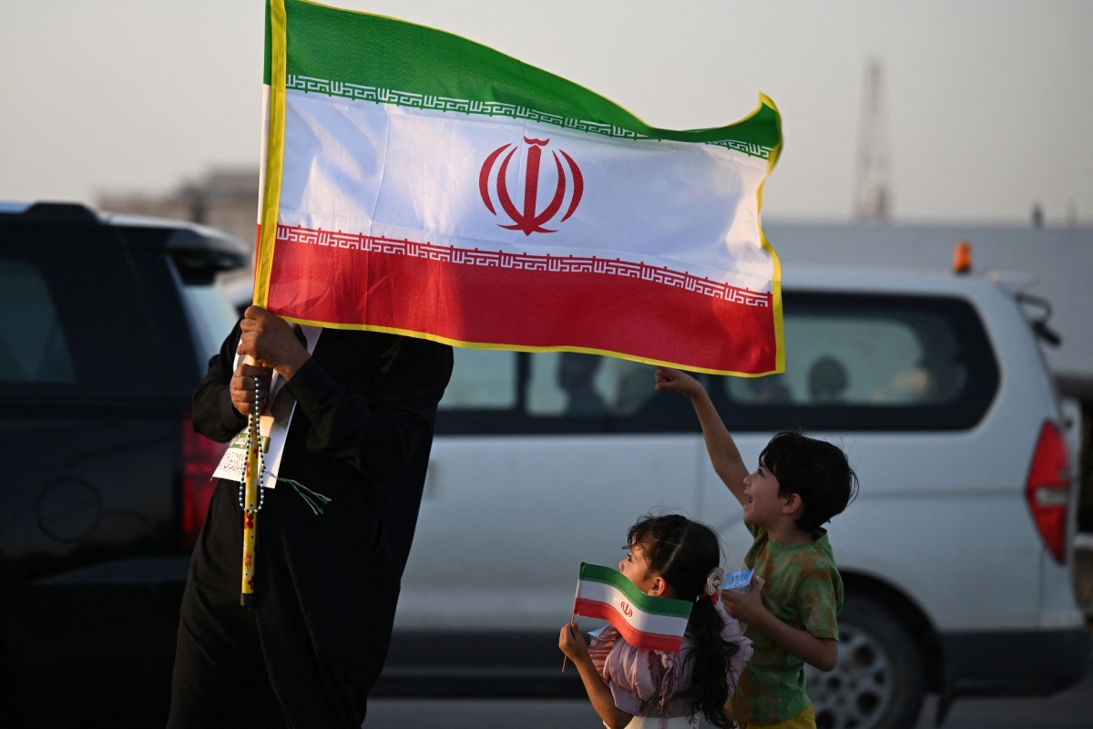 An Iraqi man and children hold Iranian flags as people march during celebrations to mark the ceasefire between Israel and Iran in the southern city of Basra on June 24, 2025.