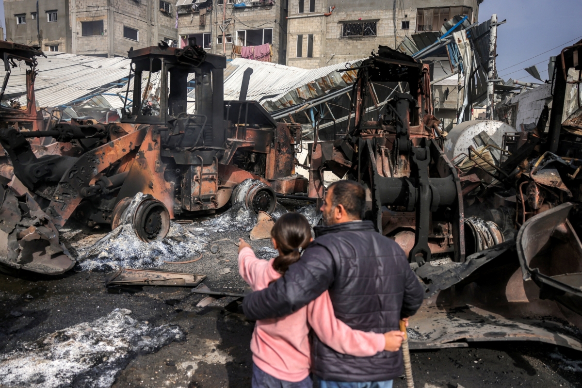 A girl stands embracing a man as they inspect destroyed bulldozers and other heavy vehicles at the Jabalia municipality garage, which was hit by Israeli bombardment, in Jabalia in the northern Gaza Strip on April 22, 2025.
