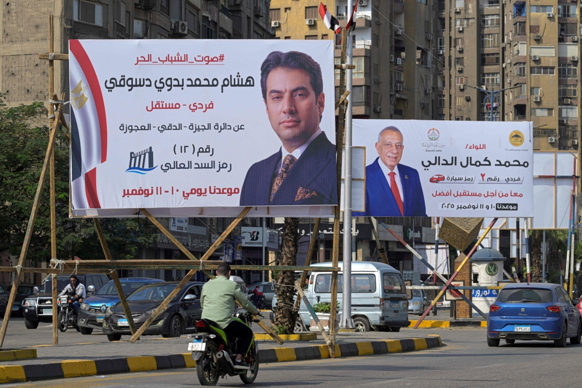 Motorists drive past a campaign billboard Egyptian Parliamentary elections candidates in the Twin Giza city of the capital Cairo on November 9, 2025, ahead of the country's parliament election starts the first round on 10 November.