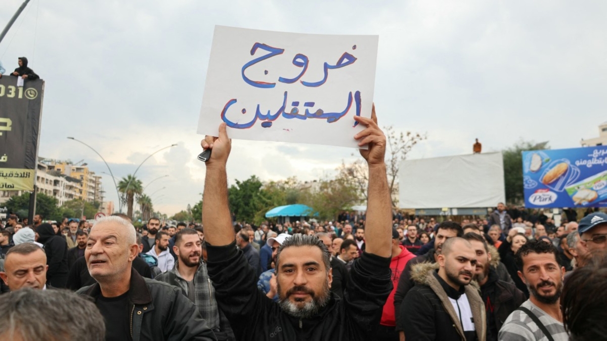A man holds up a sign that reads in Arabic, "Release of the detained", as people take part in a protest in the coastal city of Latakia in Syria's Alawite heartland on 25 November 2025.