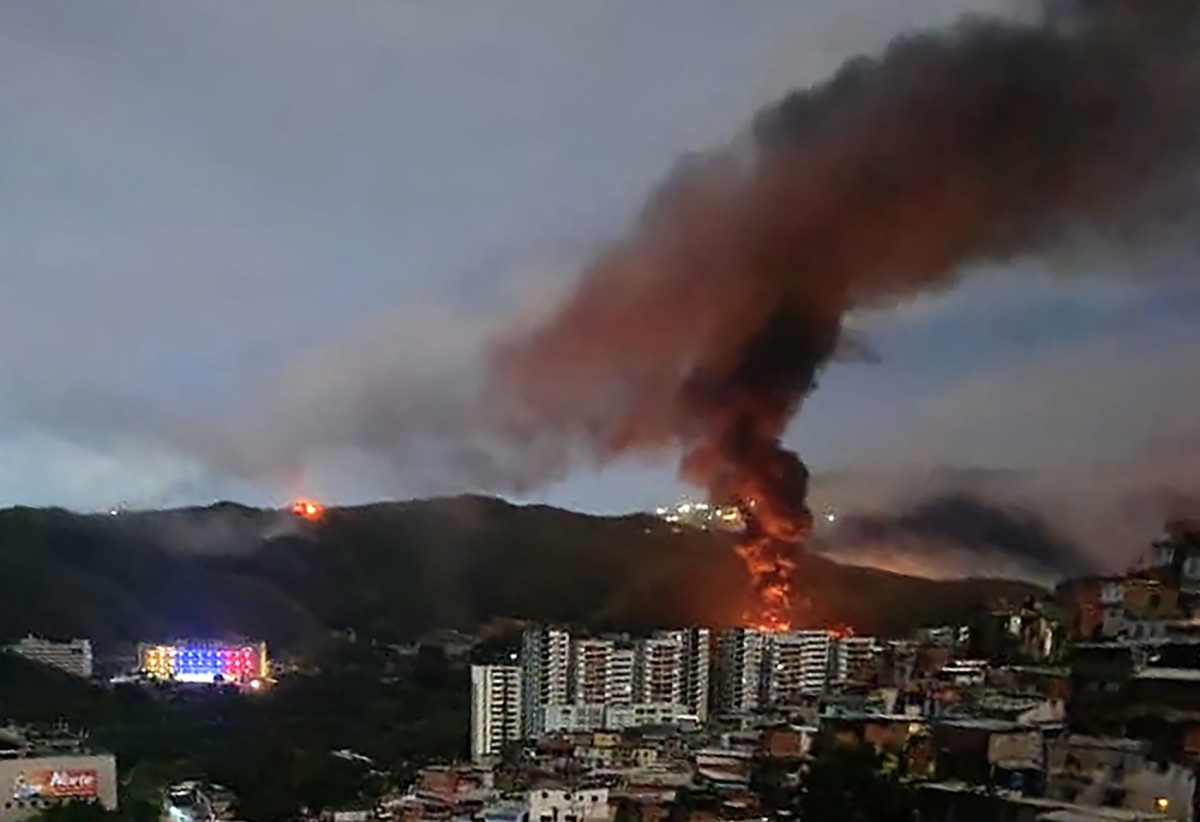 Fire at Fuerte Tiuna, Venezuela's largest military complex, is seen from a distance after a series of explosions in Caracas on 3 January 2026. 