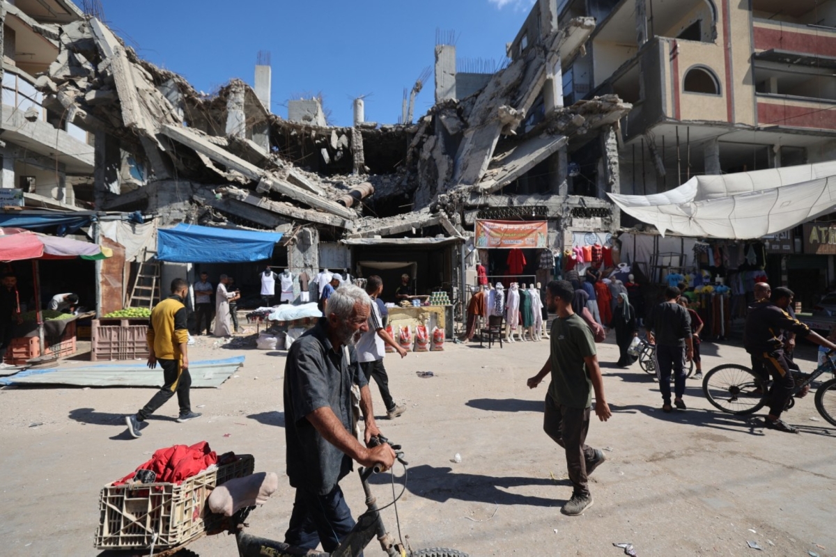 Palestinians walk past a destroyed building at a makeshift market in the Nuseirat refugee camp, located in the central Gaza Strip, on October 15, 2025, two days after a ceasefire came into effect.