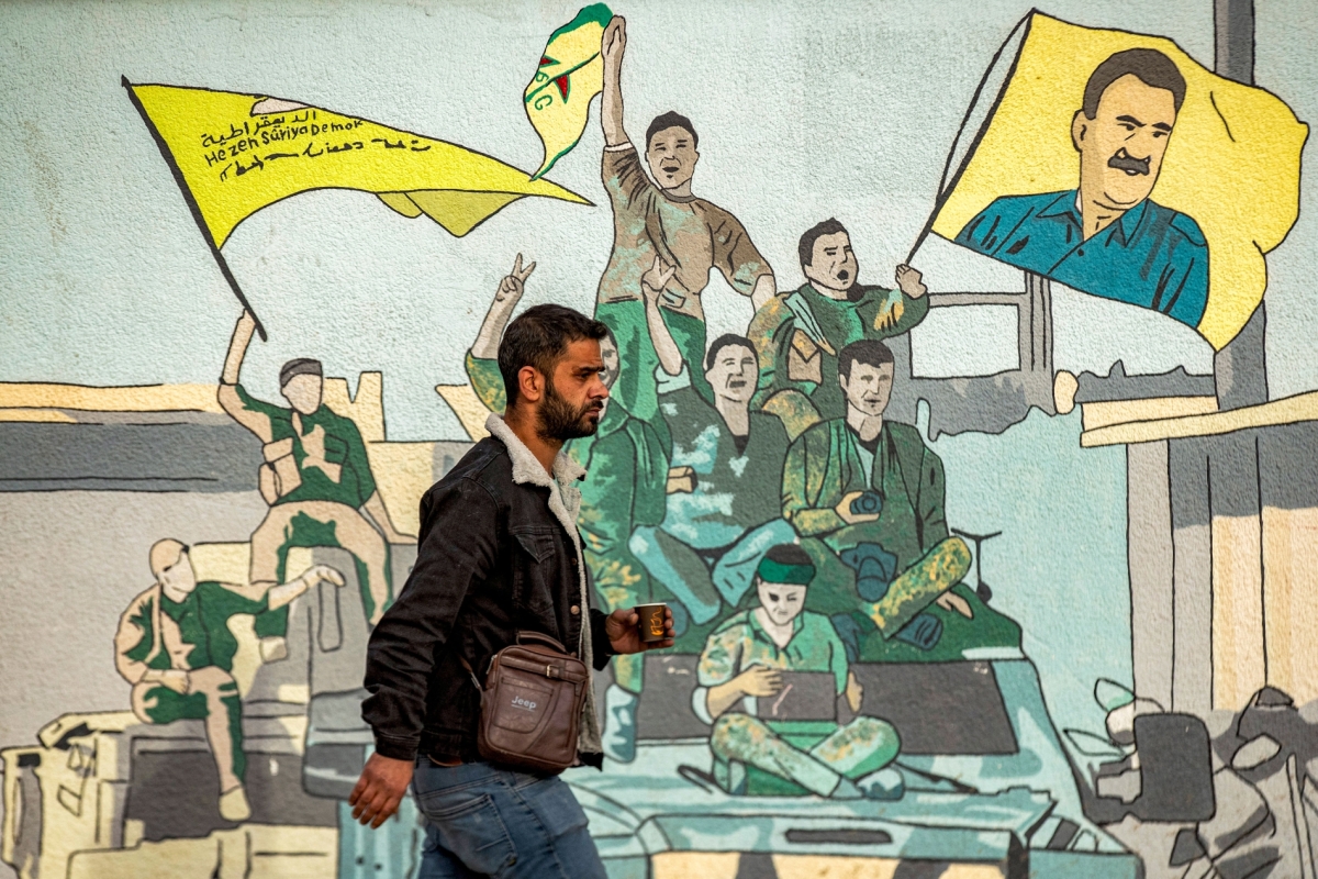 A man walks past a mural depicting SDF supporters raising a flag showing the face of Abdullah Öcalan, the founding leader of the PKK, in Syria's northeastern city of Qamishli on December 16, 2024. 