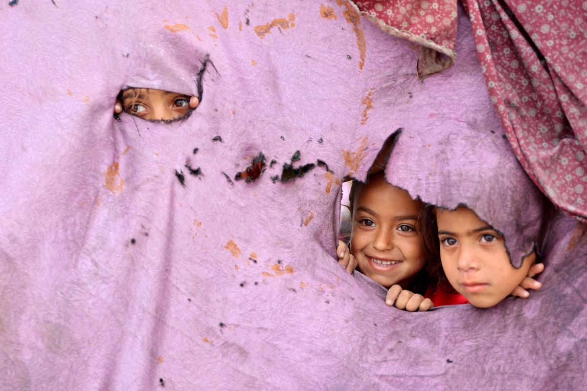 Palestinian children peek out of holes in their tent at a makeshift displacement camp set up amid building rubble in Gaza City on 12 May 2025.