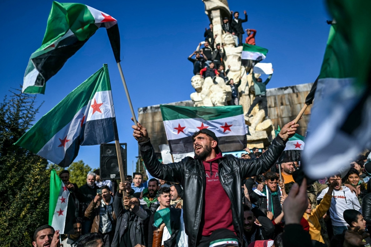 People wave independence-era Syrian flags as they gather at Saadallah al-Jabiri Square after the Friday noon prayer in Aleppo on 13 December 2024.