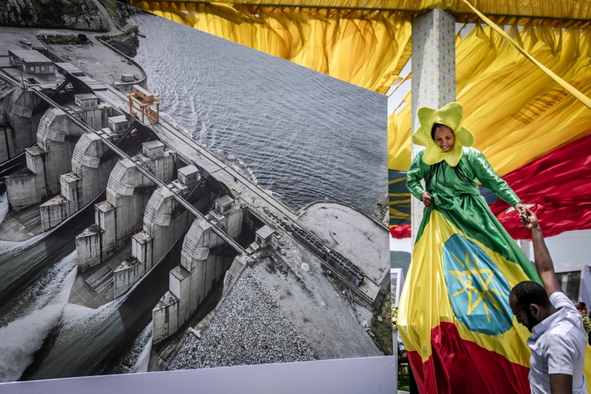 A performer stands next to a decorative aerial image of the Grand Ethiopian Renaissance Dam (GERD) during its official inauguration ceremony in Guba, on 9 September 2025. 