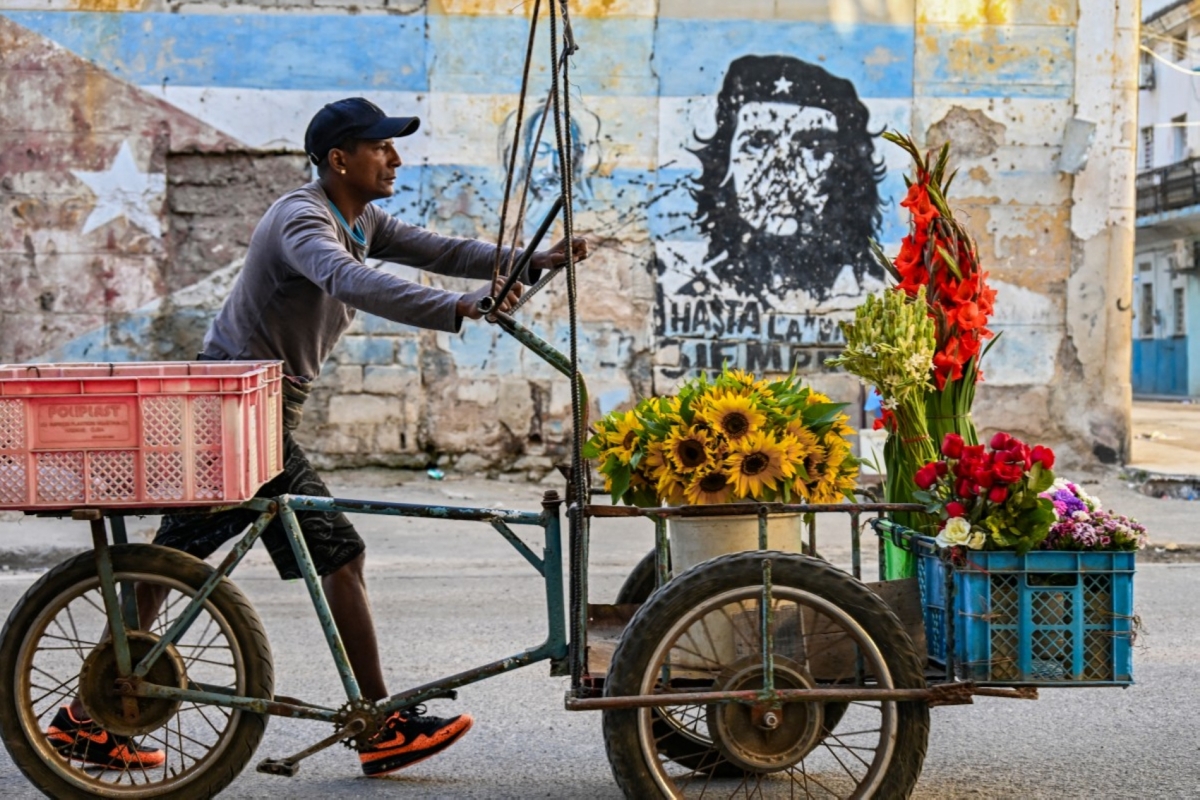 A flower street vendor pushes his cart past a mural depicting Argentine-born revolutionary leader Ernesto “Che” Guevara reading “Until victory, always” in Havana on 25 February 2026.
