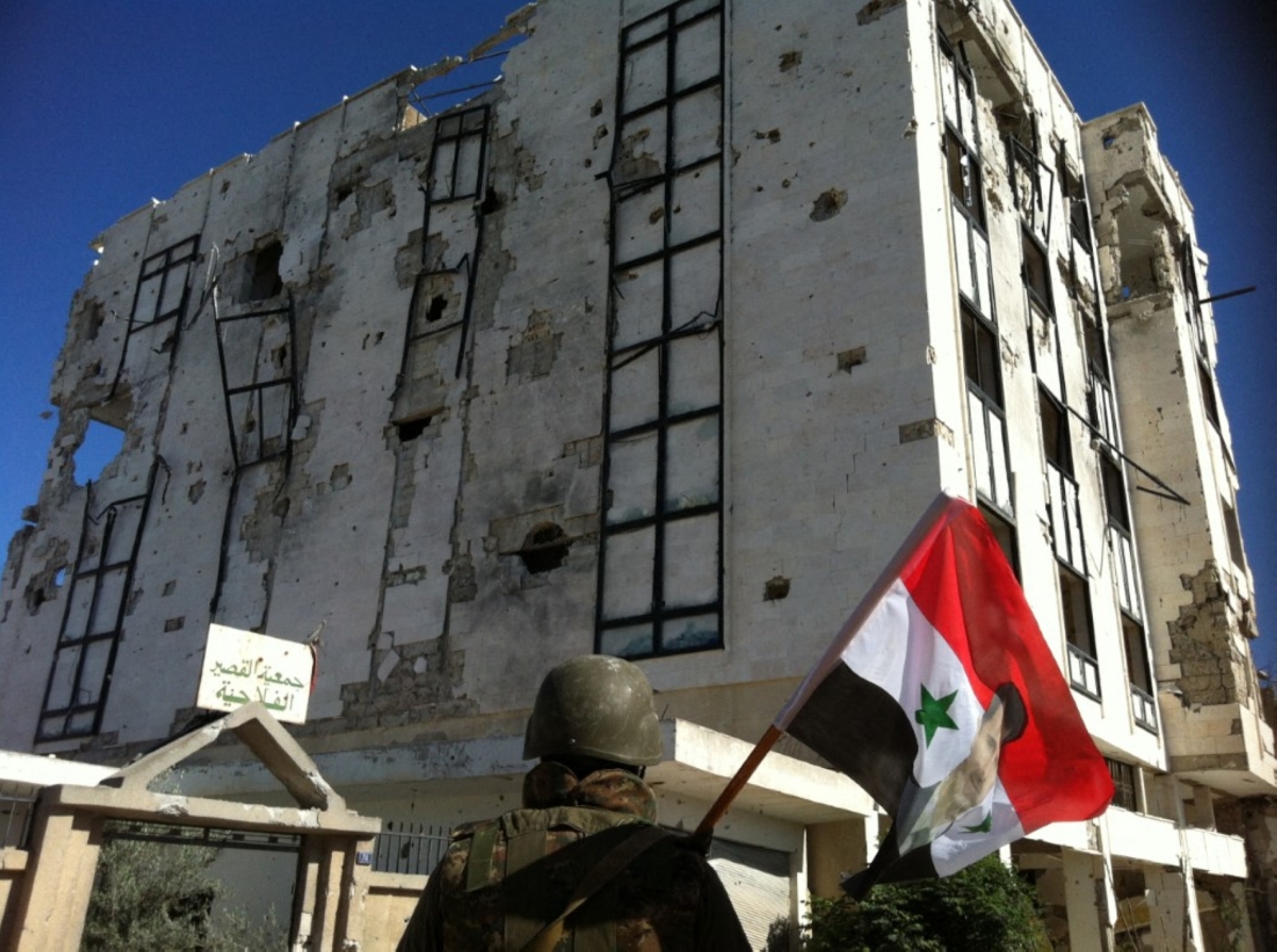 A Syrian army soldier holds a national flag featuring Syria's President Bashar al-Assad in front of a building left in ruins on 5 June 2013 in the city of Qusayr in the Homs province. 