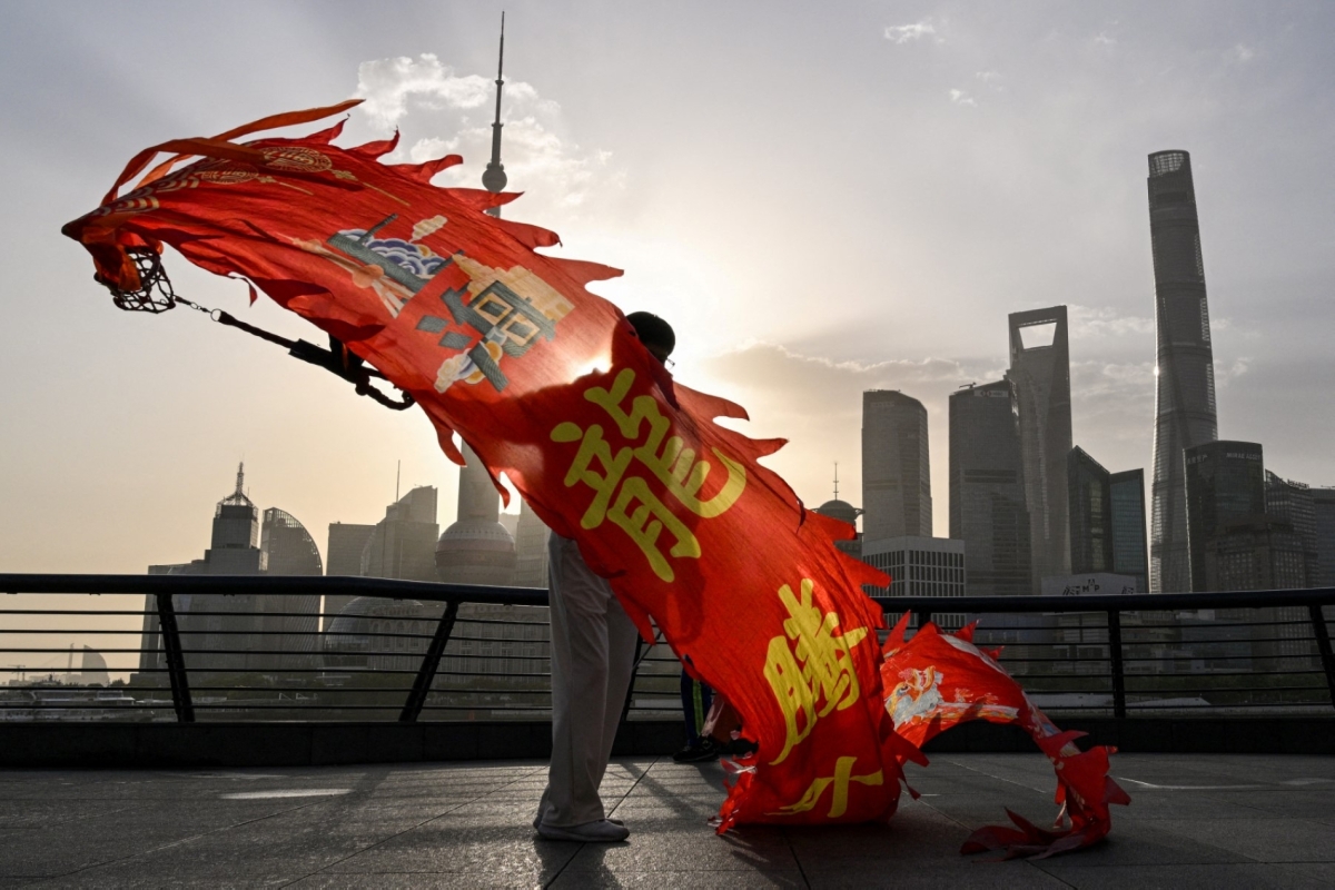 A woman twirls a dragon streamer on the Bund promenade along the Huangpu River during sunrise in Shanghai on 14 April 2025, with the city's financial district seen in the background.