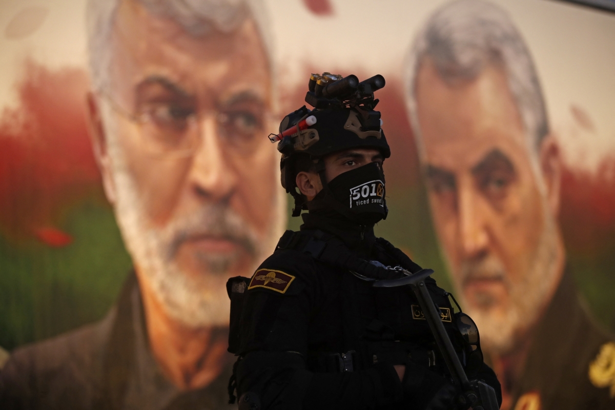 A member of Iraq's PMF stands in front of a banner depicting slain Iraqi commander Abu Mahdi al-Muhandis (L) and Iranian commander Qassem Soleimani, on January 2, 2023.