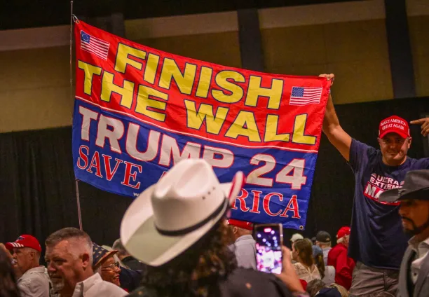 Supporters of Donald Trump hold a sign about the border wall with Mexico before Trump speaks at a campaign rally in Florida on 11 October 2023. Trump has now allocated $46bn to build it.