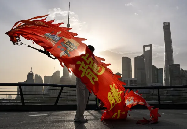 A woman twirls a dragon streamer on the Bund promenade along the Huangpu River during sunrise in Shanghai on 14 April 2025, with the city's financial district seen in the background.