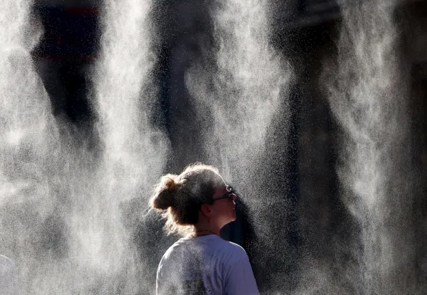 A woman cools off under a mist sprayer during the annual street music festival 'Fete de la Musique' while taking part in a heatwave in Bordeaux, southwestern France on 21 June 2026.