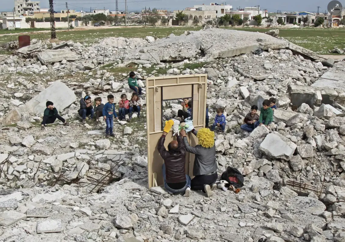 Walid Abu Rashed, wearing a yellow wig, and a fellow actor entertain children through a makeshift puppet theatre set up among the rubble of collapsed buildings in the town of Saraqib in the rebel-held northern Idlib province. (Getty)
