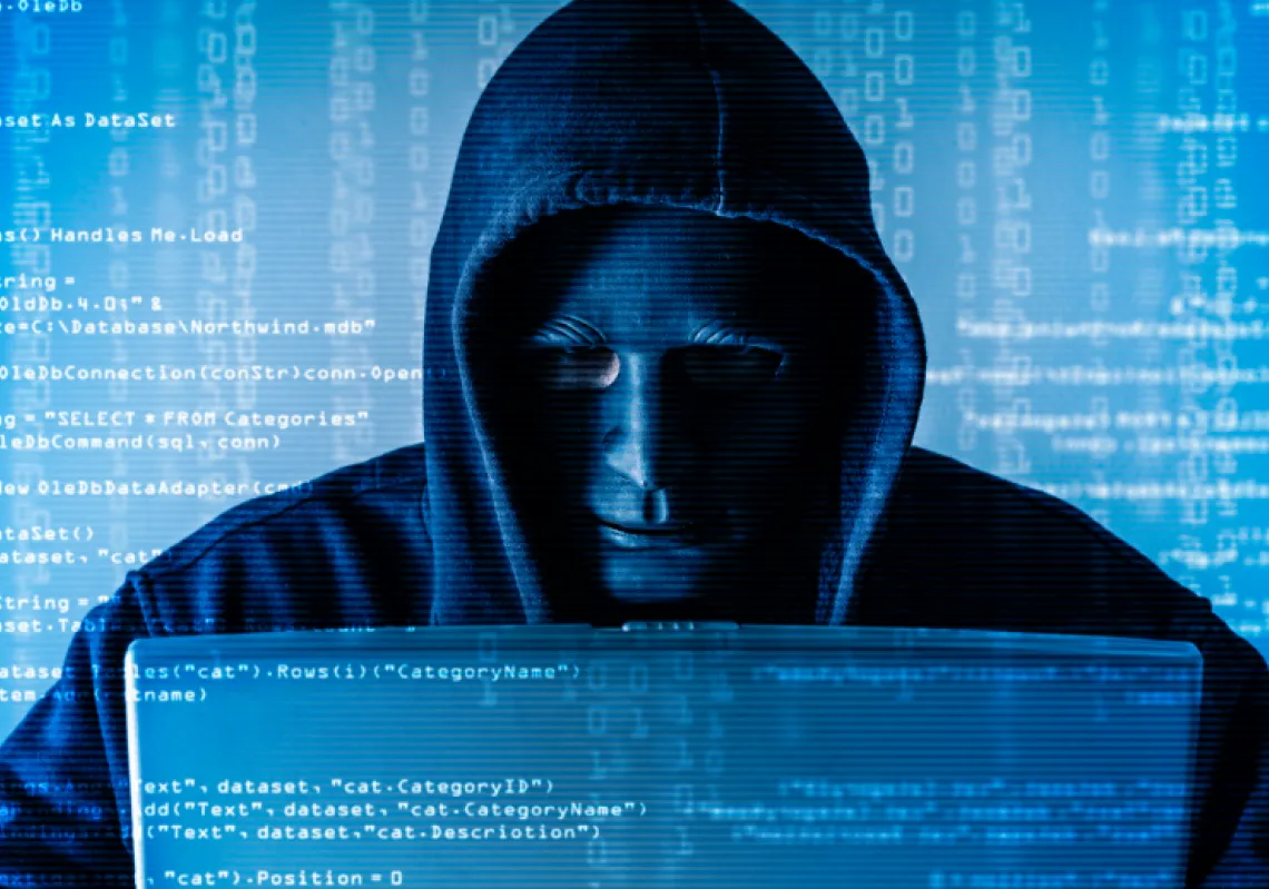 The abstract image of the hacker wearing a mask and using a laptop in the empty white room overlay with source code hologram. (Getty)