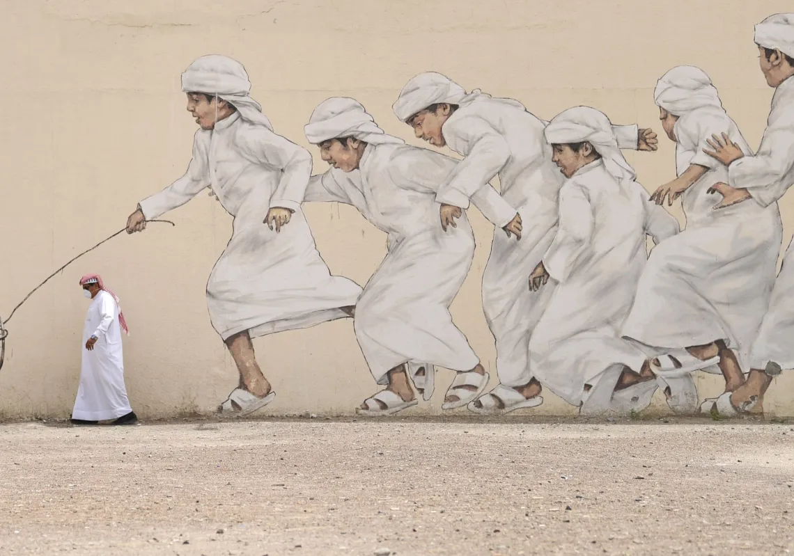 An Emirati man, wearing a protective face-mask, walks past a graffiti in Dubai on March 28, 2020.(Getty)