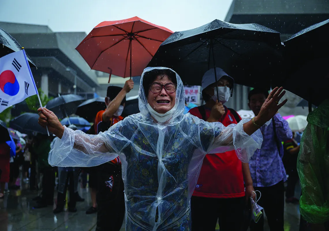  A woman weeps as members of pro-US conservative right-wing and religious christian groups wave flags and shout slogans during an anti-government rally in the central Gwanghwamun area of Seoul on August 15, 2020. (Getty)