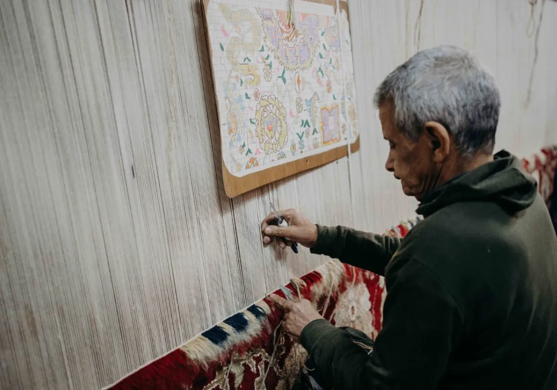 A weaver sitting at a loom, working knot-by-knot to duplicate the pattern printed on the paper in front of him, in al-Kattan Factory in Cairo, Egypt. (Supplied)