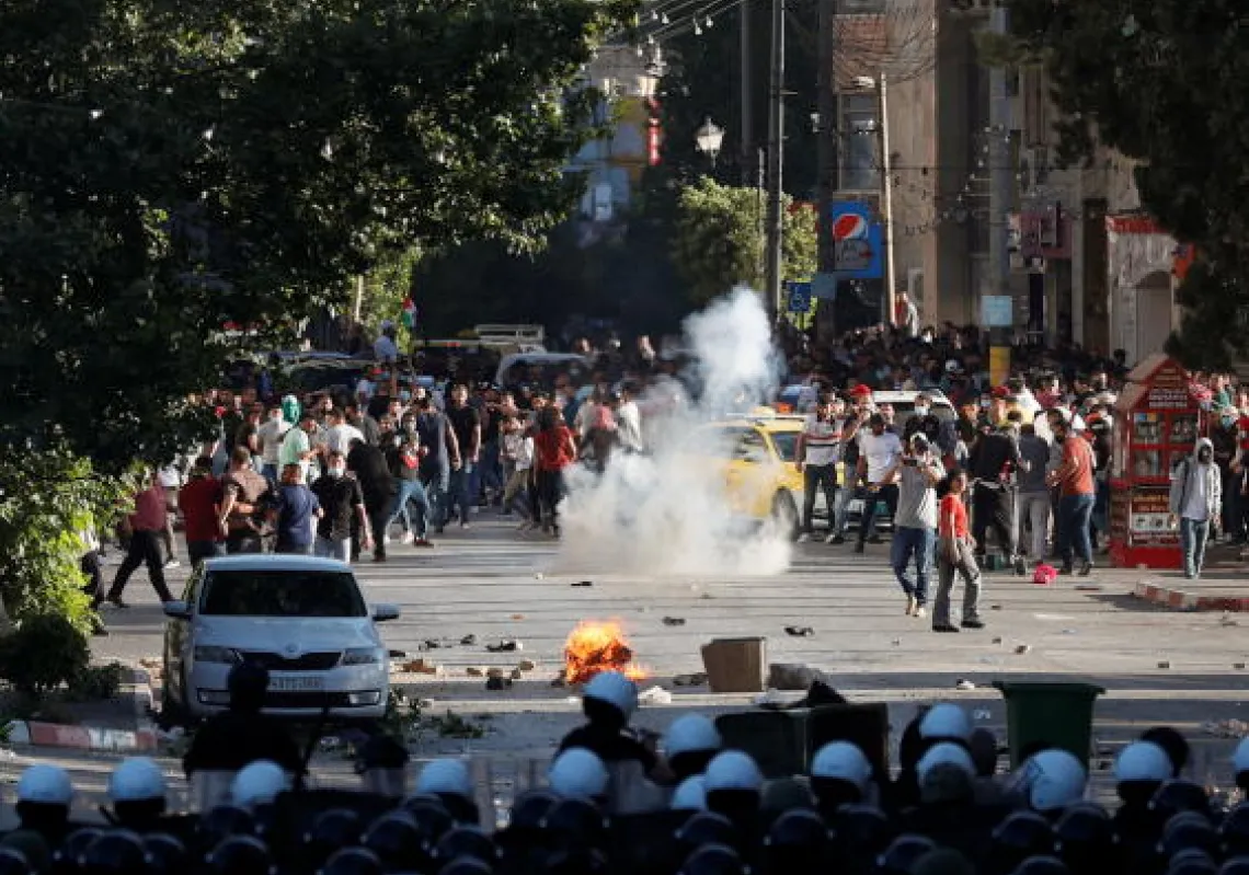 A fire burns between a formation of Palestinian police officers and demonstrators during a protest over the death of Nizar Banat, a critic of the Palestinian Authority, in Ramallah in the Israeli-occupied West Bank, June 26, 2021.(Reuters)