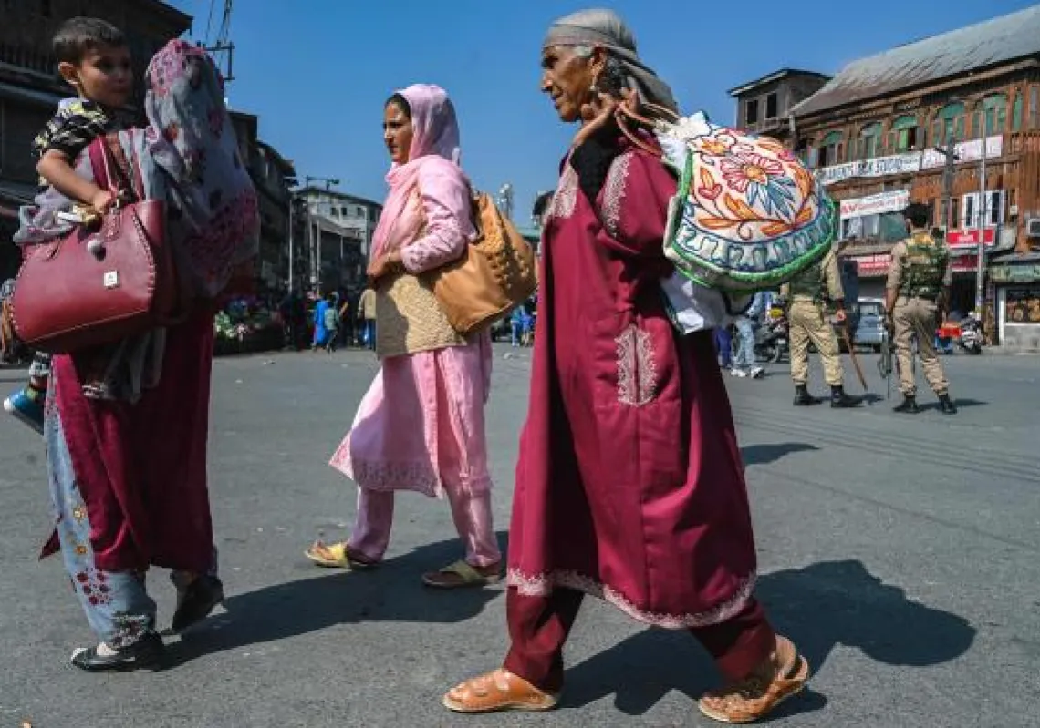 Pedestrians walk past security personnel standing on guard along a street in Srinagar on October 9, 2021, after recent attacks by the suspected anti-India militants in Indian-administered Kashmir. (Photo by Tauseef MUSTAFA / AFP)