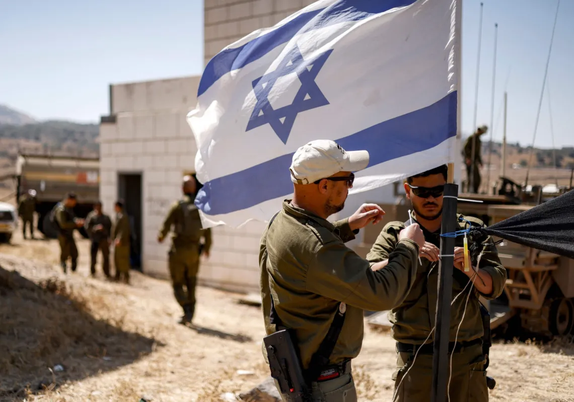Israeli army soldiers add zip ties to the mast of an Israeli flag flying at a special area for exercises during a military drill in the Israeli-annexed Golan Heights on July 8, 2025.