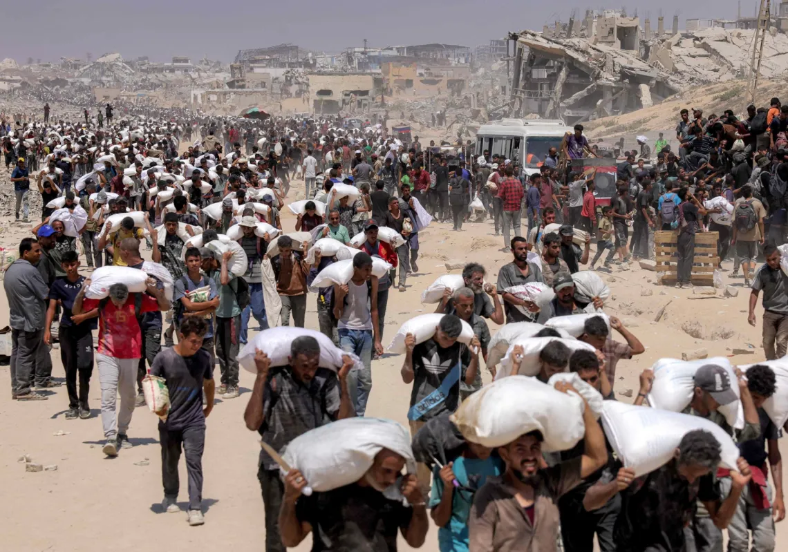 غزيون يحملون الطحين على أكتافهم قرب معبر زيكيم في شمال غزة في 27 يوليو 2025