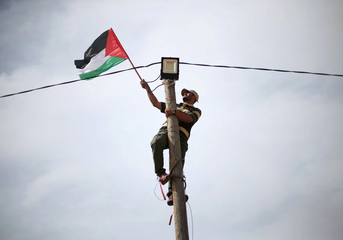 A man hangs a Palestinian flag at an electric pole near the border with Israel, in the southern Gaza Strip, before the recent war that has knocked out most of the territory's infrastructure.
