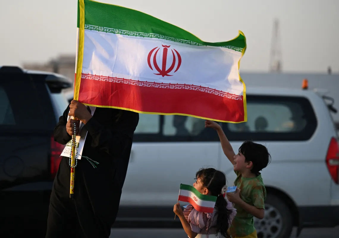 An Iraqi man and children hold Iranian flags as people march during celebrations to mark the ceasefire between Israel and Iran in the southern city of Basra on June 24, 2025.