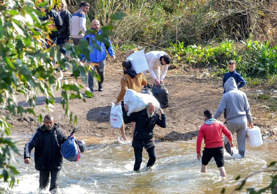 عائلات من الطائفة العلوية في سوريا تعبر نهر الكبير الذي يشكل الحدود بين الساحل السوري الجنوبي ولبنان، في منطقة حكر الضاهري، بتاريخ 11 آذار/مارس 2025، للدخول إلى لبنان هرباً من أعمال عنف طائفية في معقلهم على الساحل السوري