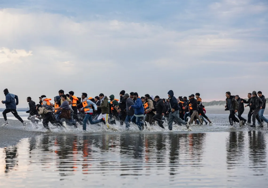 Migrants run to board a smuggler's boat in an attempt to cross the English Channel off the beach of Gravelines, northern France, on August 12, 2025.