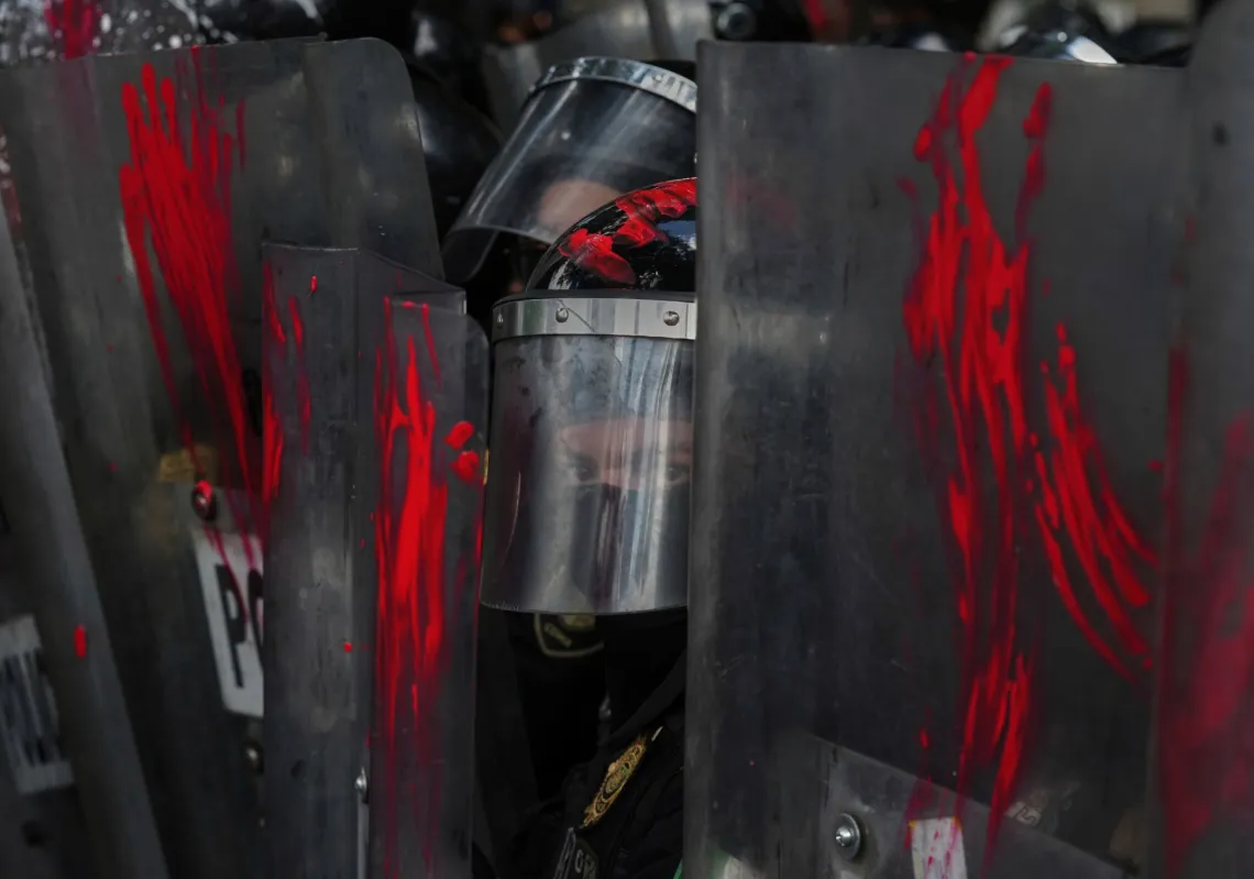 A police officer looks out from shields on which demonstrators smeared paint at a protest against the war in Gaza, in Mexico City, Sunday, August 17, 2025. 