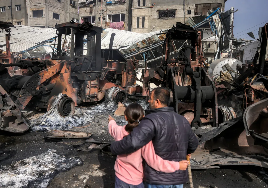 A girl stands embracing a man as they inspect destroyed bulldozers and other heavy vehicles at the Jabalia municipality garage, which was hit by Israeli bombardment, in Jabalia in the northern Gaza Strip on April 22, 2025.