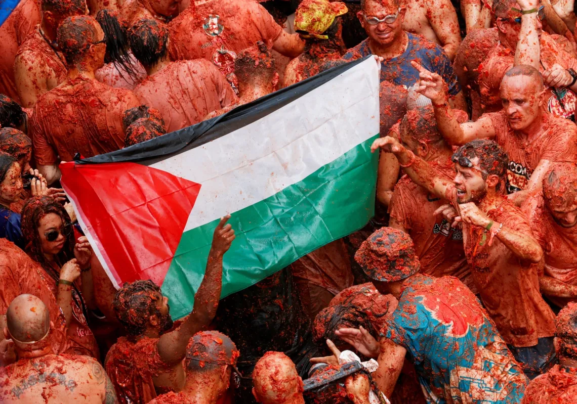 Revellers covered in tomato pulp carry a Palestinian flag during the annual 'La Tomatina' food fight festival in Bunol, near Valencia, Spain, on August 27, 2025. 