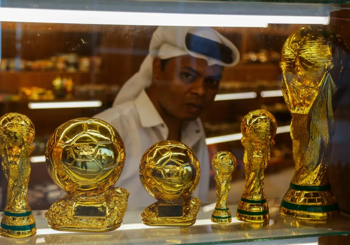 A shopkeeper looks out through a window displaying replicas of football trophies at a gift shop in Souq Waqif bazaar in Doha on July 24, 2025. 