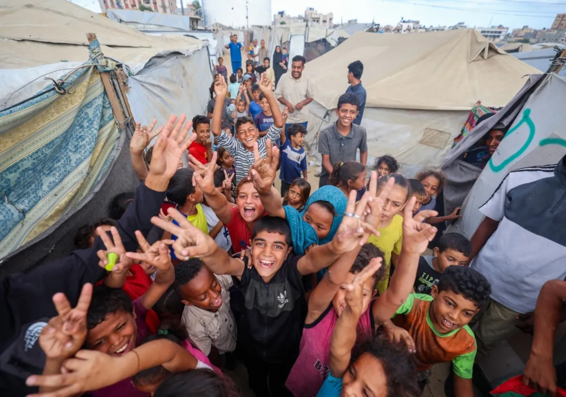 أطفال فلسطينيون يحتفلون في مخيم للنازحين في النصيرات وسط قطاع غزة في 9 أكتوبر 2025، بعد أنباء عن اتفاق وقف إطلاق النار الجديد في غزة