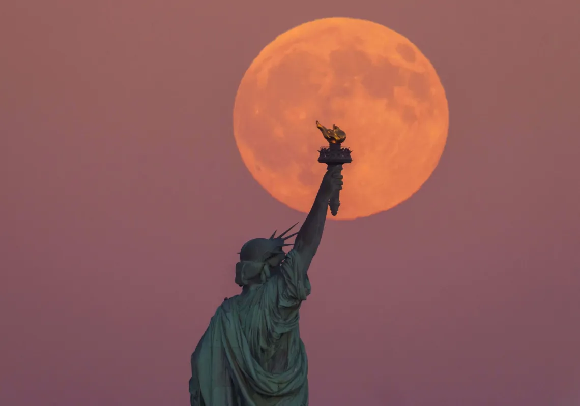 The Harvest Supermoon rises behind the Statue of Liberty and the Brooklyn skyline, on Monday, October 6, 2025, in Jersey City, New Jersey.