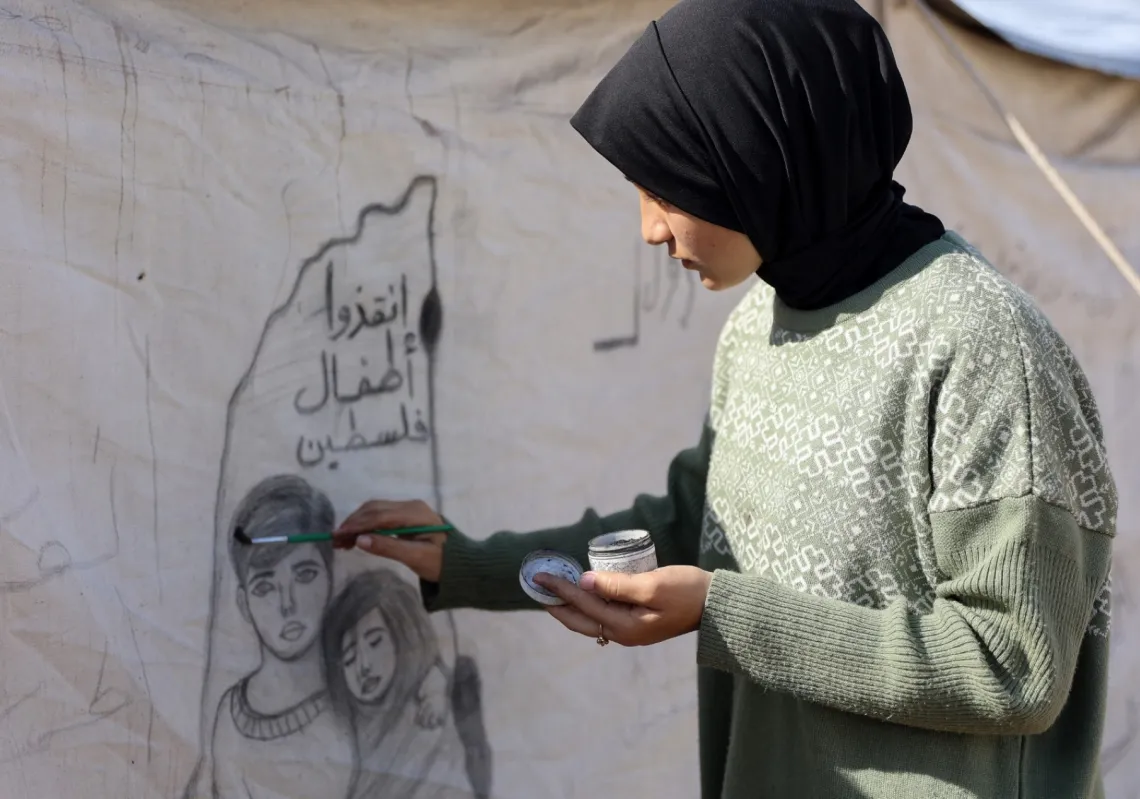 Israa Saada (17 years old) draws on a tent in a displaced persons camp in Gaza.