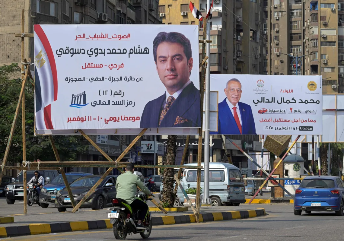 Motorists drive past a campaign billboard Egyptian Parliamentary elections candidates in the Twin Giza city of the capital Cairo on November 9, 2025, ahead of the country's parliament election starts the first round on 10 November.