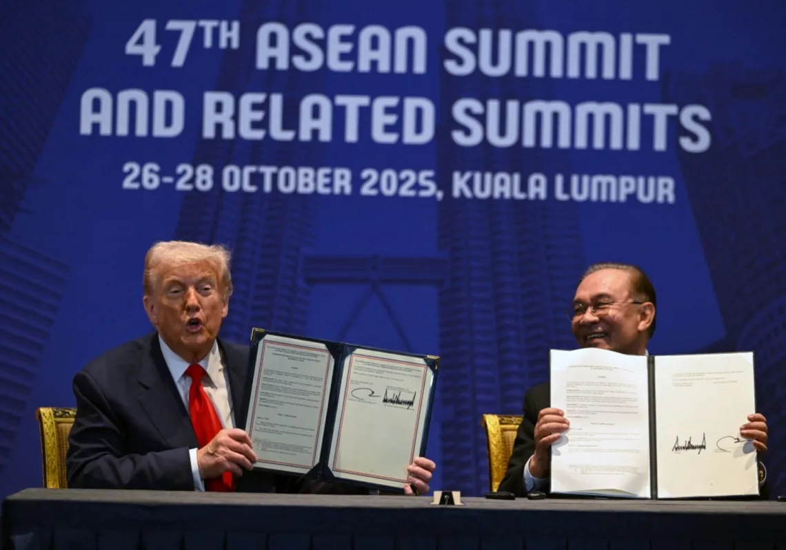 US President Donald Trump (L) and Malaysia's Prime Minister Anwar Ibrahim (R) hold up signed documents on a trade deal during a bilateral meeting on the sidelines of the 47th ASEAN Summit in Kuala Lumpur on 26 October 2025. 