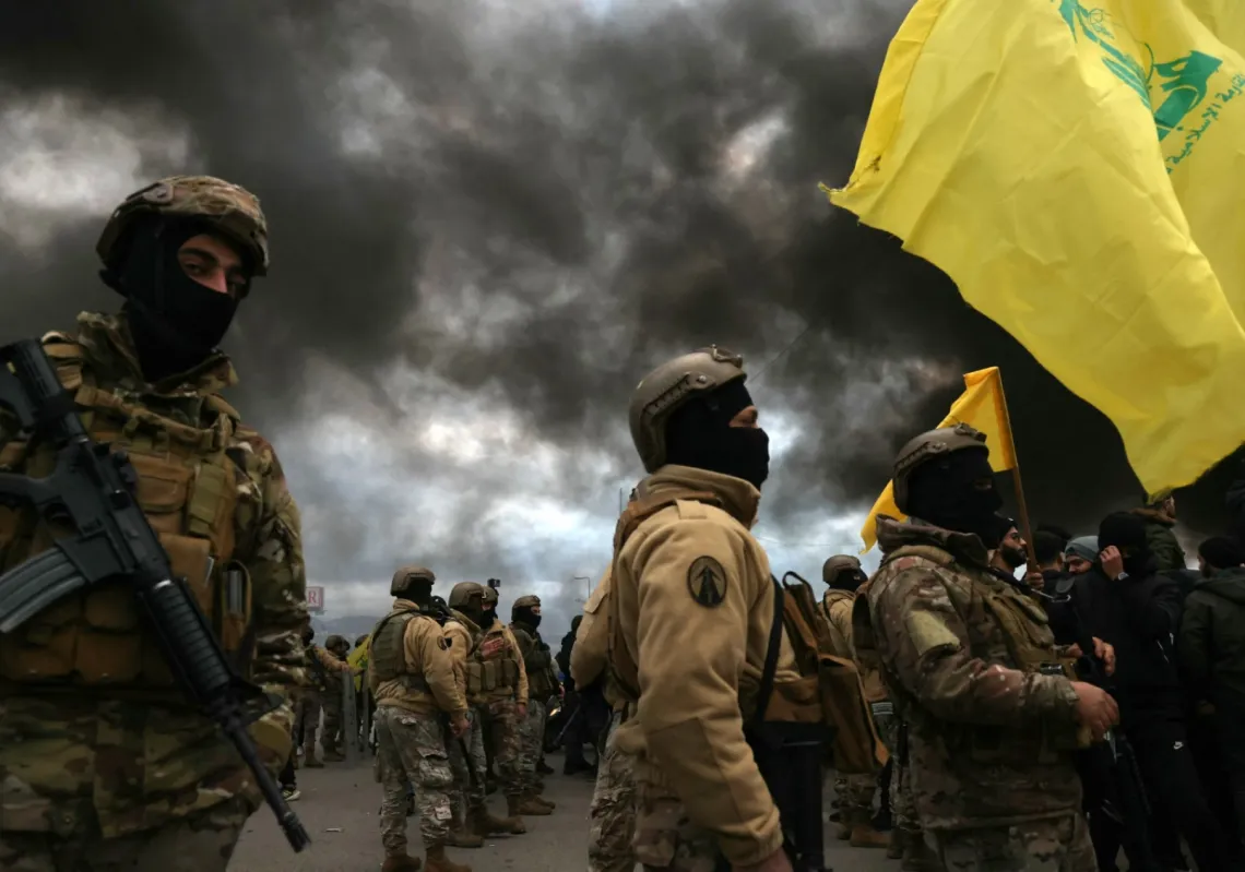 أحد مناصري "حزب الله" يلوح بعلم الحزب أمام عناصر الجيش اللبناني خلال إغلاق الطريق المؤدي إلى مطار بيروت الدولي،  في 7 فبراير 2025