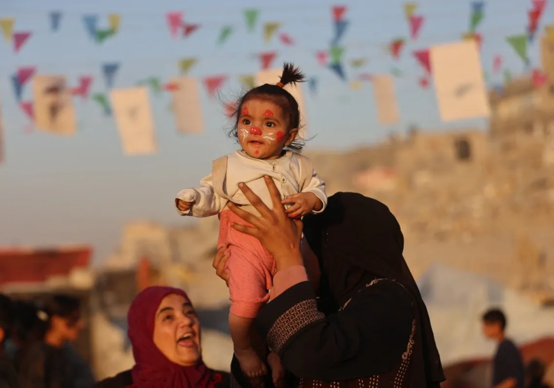نازحة تحمل طفلا خلال فعالية سينمائية للأطفال في مخيم الشاطئ، 23 نوفمبر 2025