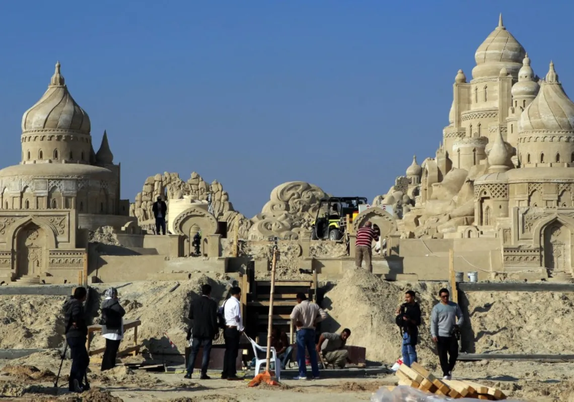 يعمل رجال على نحت رملي في قرية الرمال بأرض المعارض في مشرف، الكويت، في ١٣ يناير ٢٠١٤، ضمن مشروع يحمل ثيمة "ألف ليلة وليلة" ويعدّ من أكبر القرى الرملية في العالم