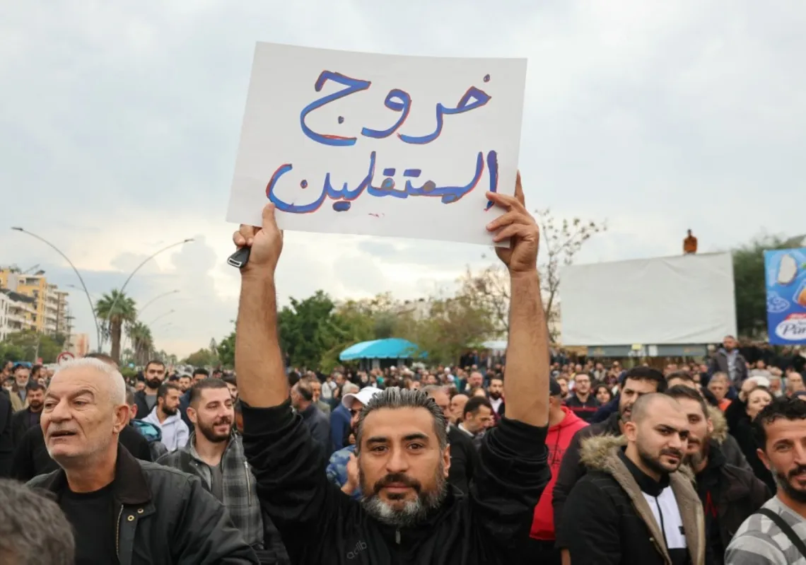 A man holds up a sign that reads in Arabic, "Release of the detained", as people take part in a protest in the coastal city of Latakia in Syria's Alawite heartland on 25 November 2025.