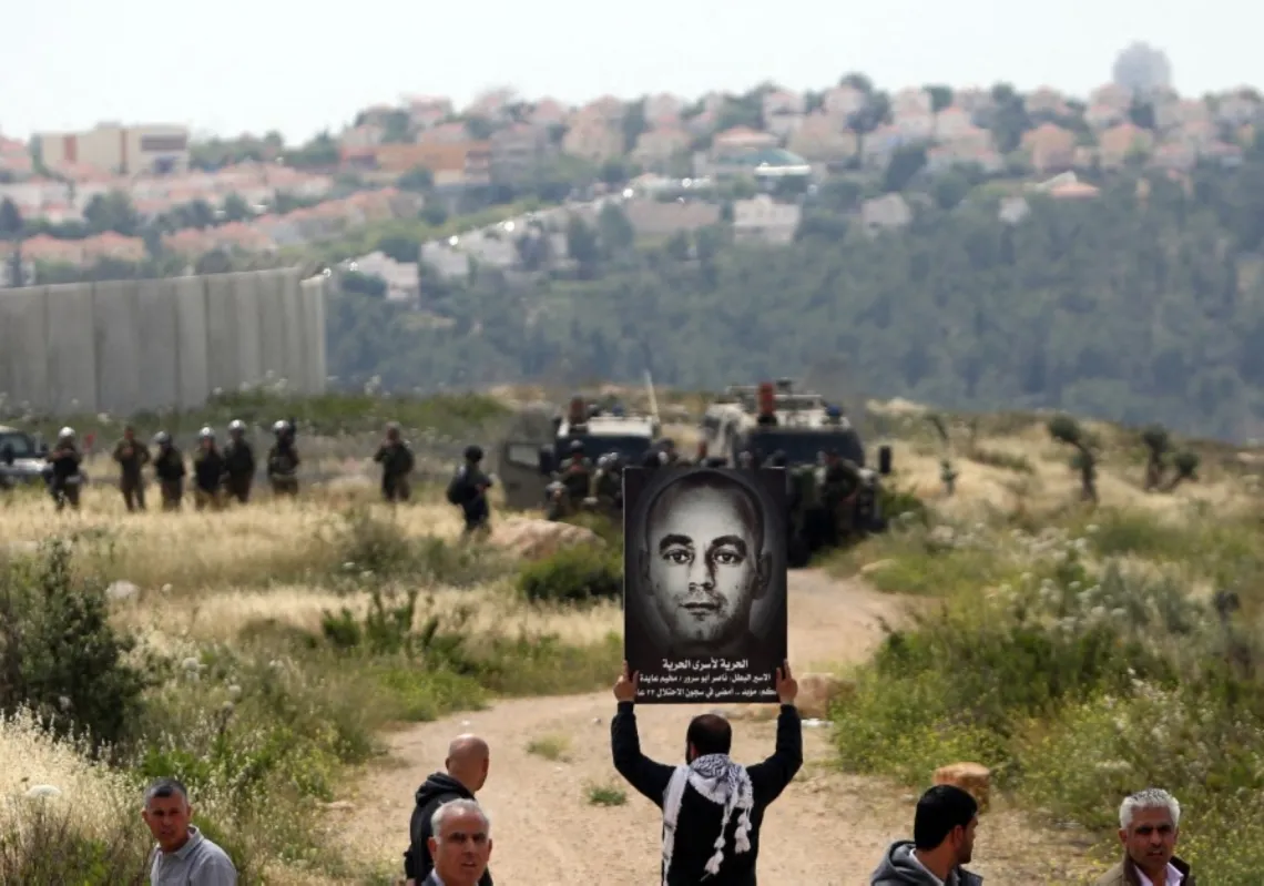 متظاهر فلسطيني يحمل لافتة عليها صورة الأسير ناصر أبو سرور خلال إحياء يوم الأسير الفلسطيني في بلعين قرب رام الله، 17 أبريل 2015