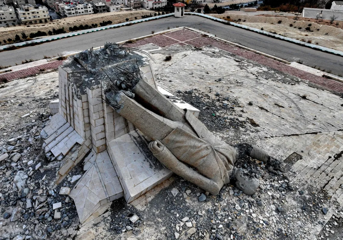 
صورة مشوهة للرئيس السوري الراحل حافظ الأسد، تعلو مبنىً أمنياً حكومياً مُدمّراً في دمشق، 8 ديسمبر 2024