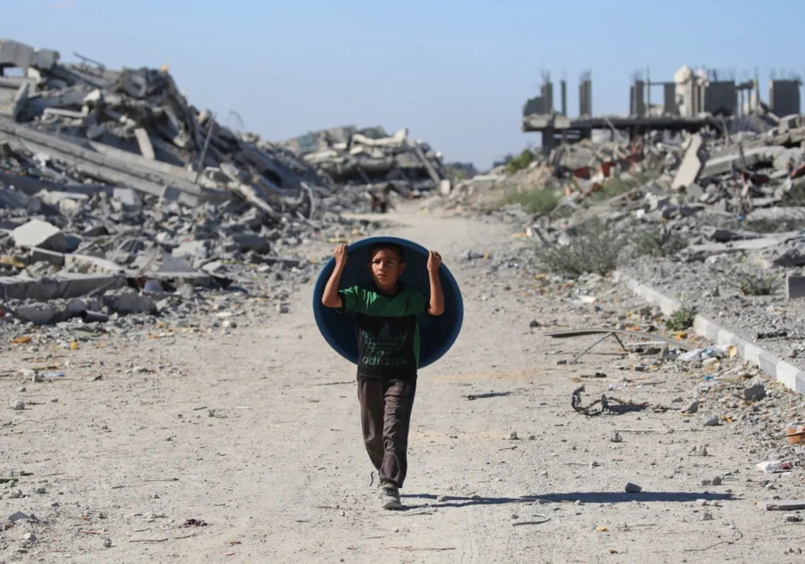 طفل يحمل حوضا بلاستيكيا أثناء عودة النازحين إلى منازلهم في منطقة الزهراء، شمال مخيم النصيرات للاجئين وسط قطاع غزة، بعد يوم من دخول وقف إطلاق النار حيز التنفيذ، في 14 أكتوبر 2025