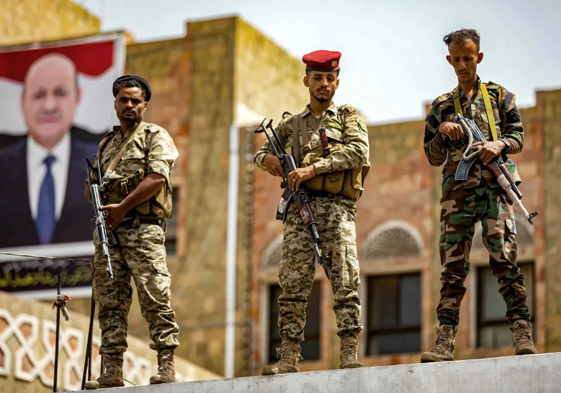  جنود موالون للحكومة اليمنية في عدن يقفون حراسا أمام لوحة تحمل صورة رئيس المجلس الرئاسي، رشاد العليمي، خلال مظاهرة تطالب بإنهاء الحصار المفروض منذ سنوات من قبل الحوثيين على مدينة تعز، في 25 مايو 2022