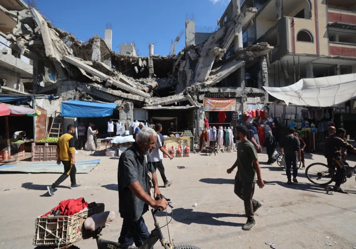 Palestinians walk past a destroyed building at a makeshift market in the Nuseirat refugee camp, located in the central Gaza Strip, on October 15, 2025, two days after a ceasefire came into effect.
